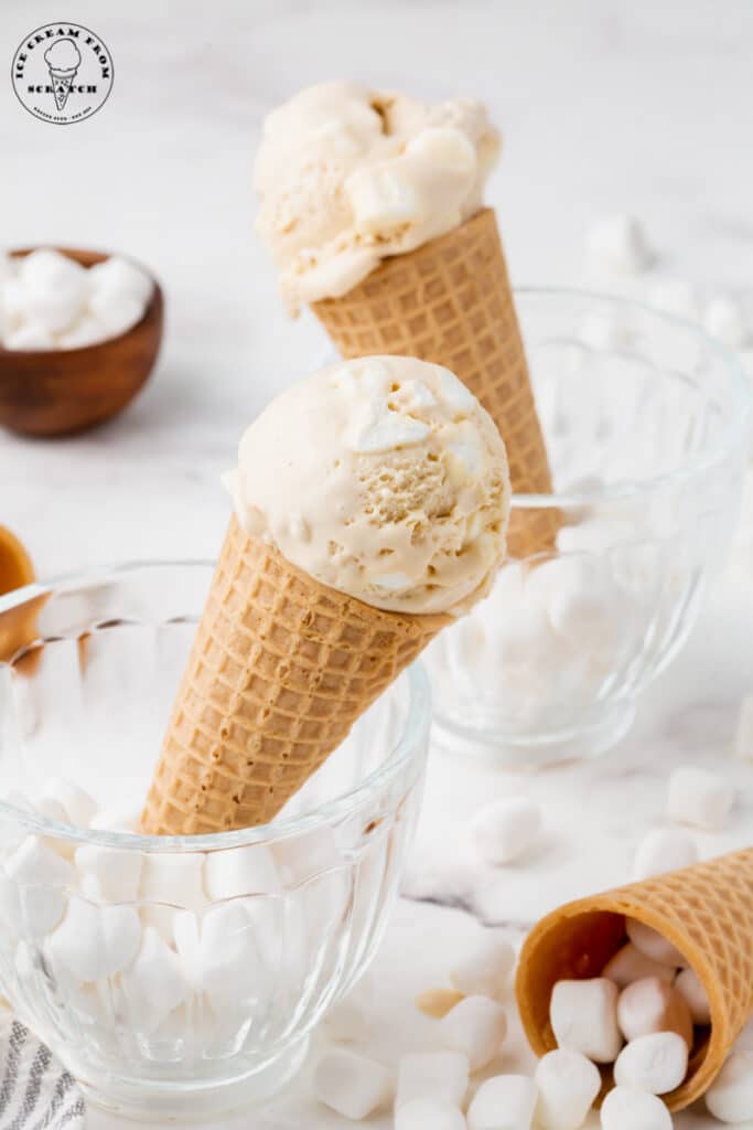 two sugar cones of marshmallow ice cream set in glass mugs filled with mini marshmallows.