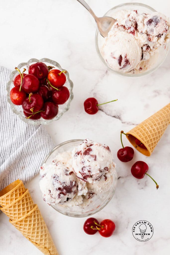 cherry vanilla ice cream in a bowl next to cherries and ice cream cones