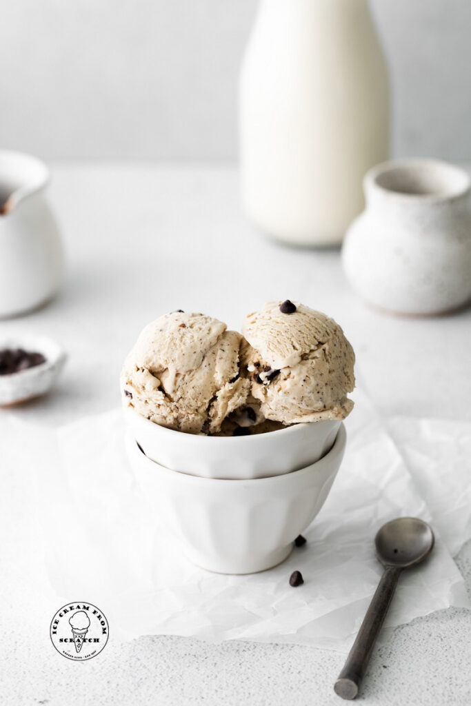 two scoops coffee flavored ice cream in a white bowl next to a spoon