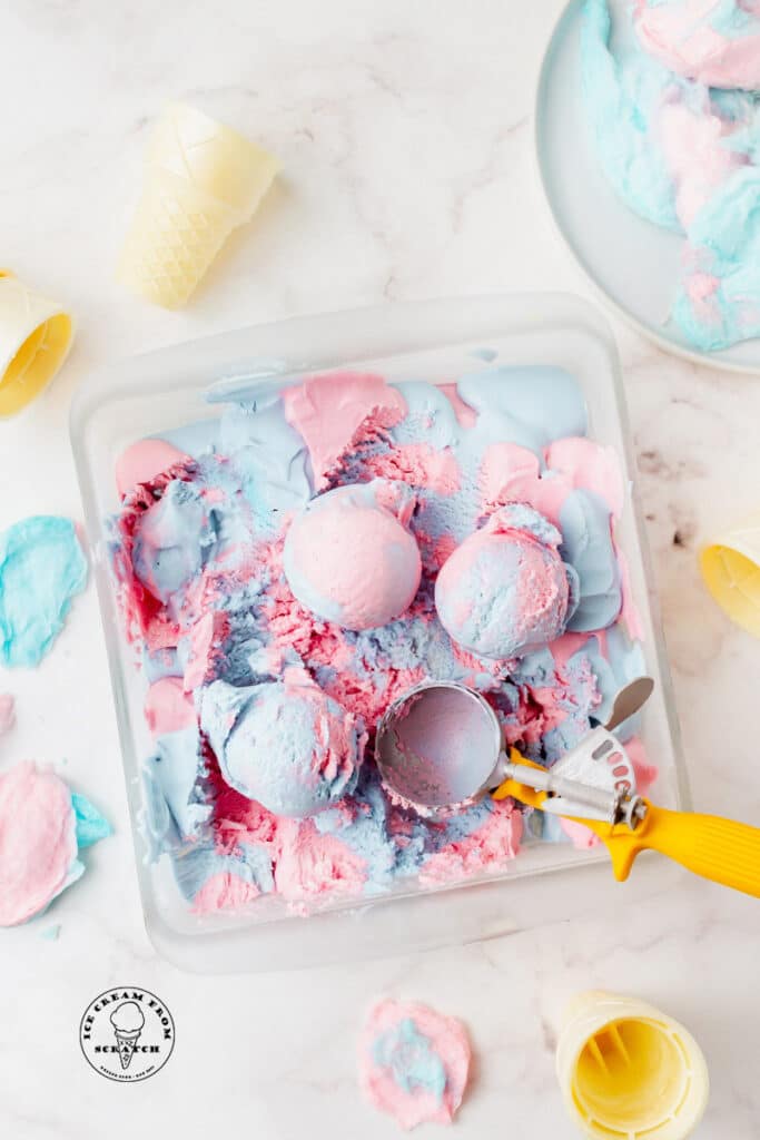 scoops of cotton candy ice cream in a glass pan with a scooper