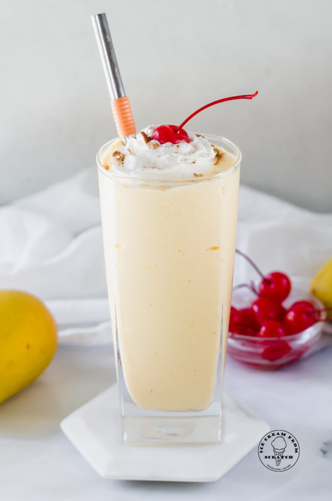 mango milkshake in a glass with a cherry and metal straw