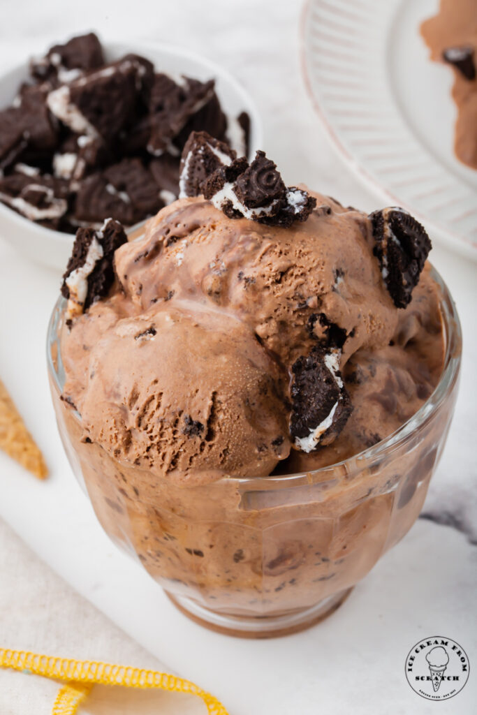 a glass ice cream dish filled with chocolate mississippi mud ice cream topped with crushed oreos.