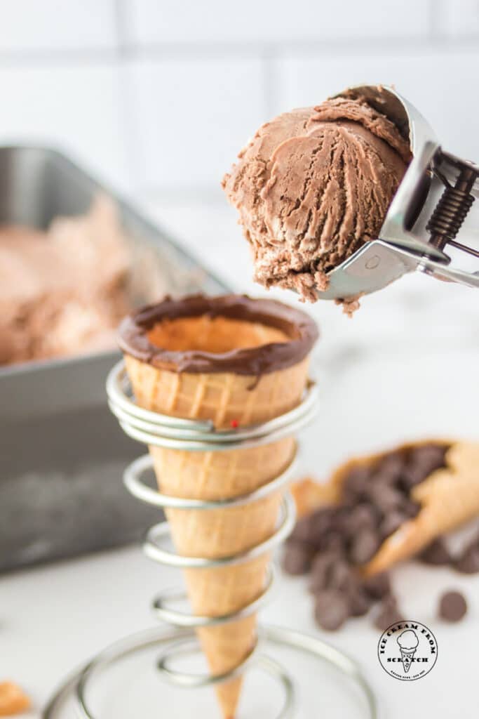 a chocolate dipped sugar cone in a silver cone holder with a scoop of chocolate ice cream being added on top.