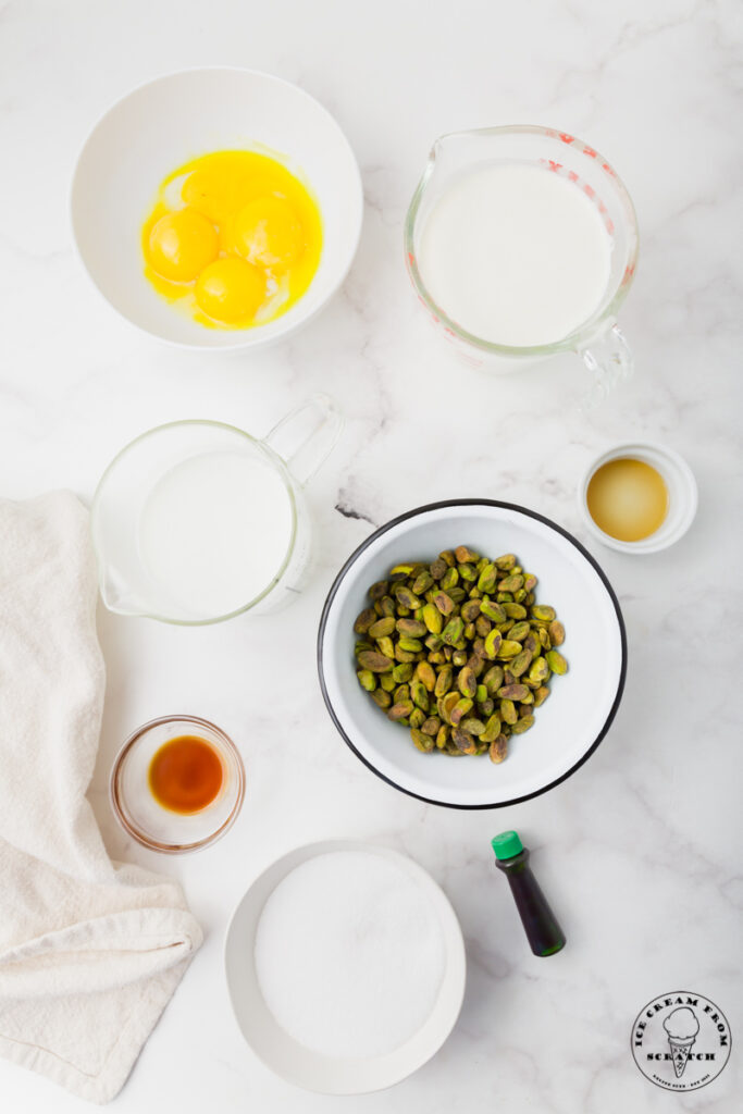 Ingredients needed for pistachio ice cream, each in separate bowls on a marble countertop.