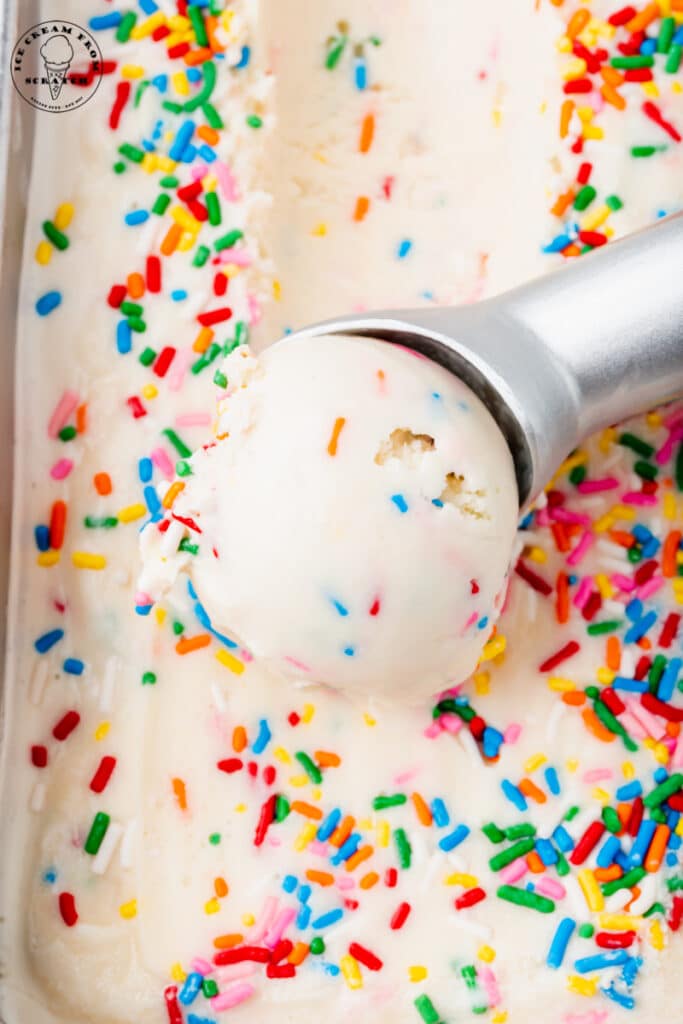 a silver ice cream scoop scooping into vanilla ice cream with sprinkles.