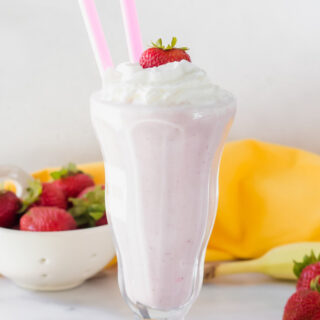 strawberry banana milkshake in a tall glass with two straws