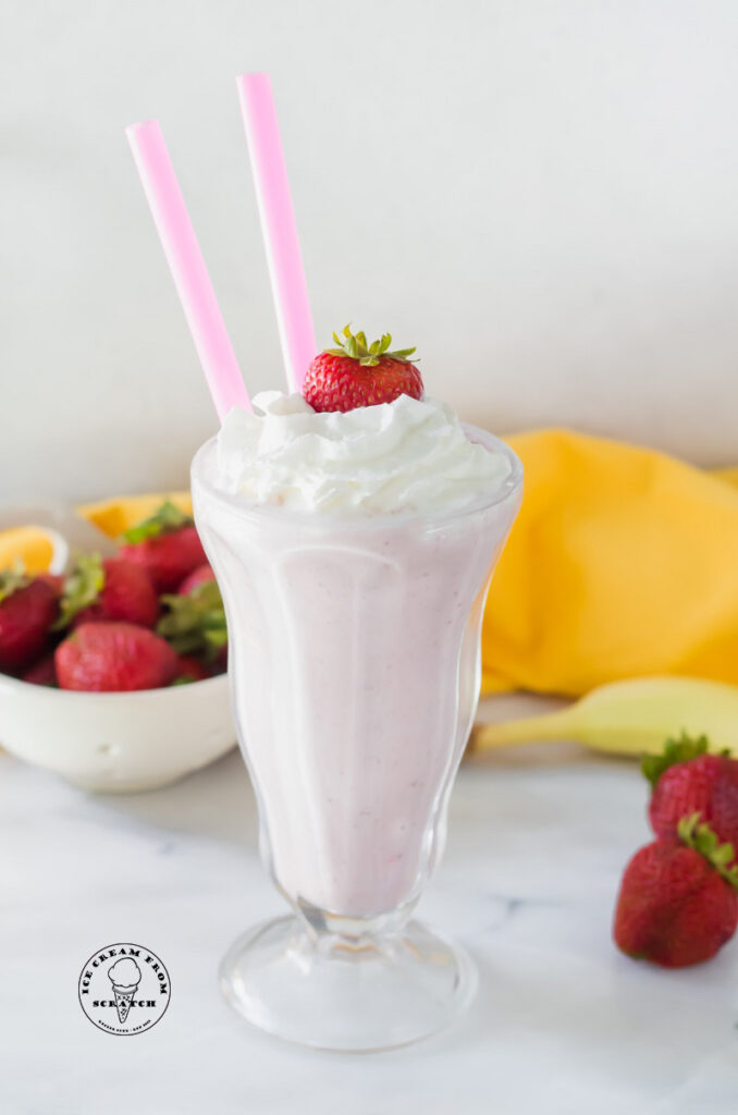 close up of a strawberry banana milkshake in a tall glass with two straws
