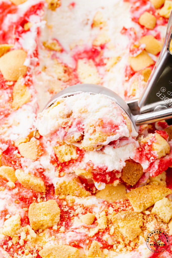 strawberry shortcake ice cream in a container topped with cookie pieces, being scooped with a silver ice cream scoop