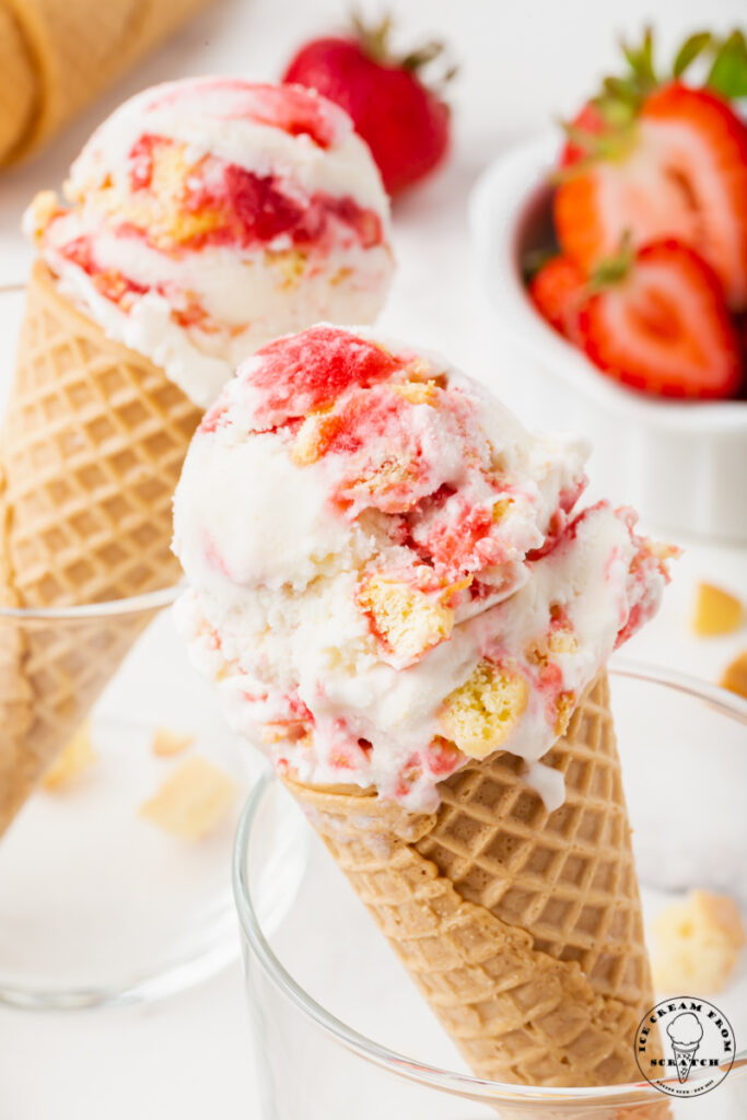 two glasses holding up sugar cones filled with strawberry shortcake ice cream.