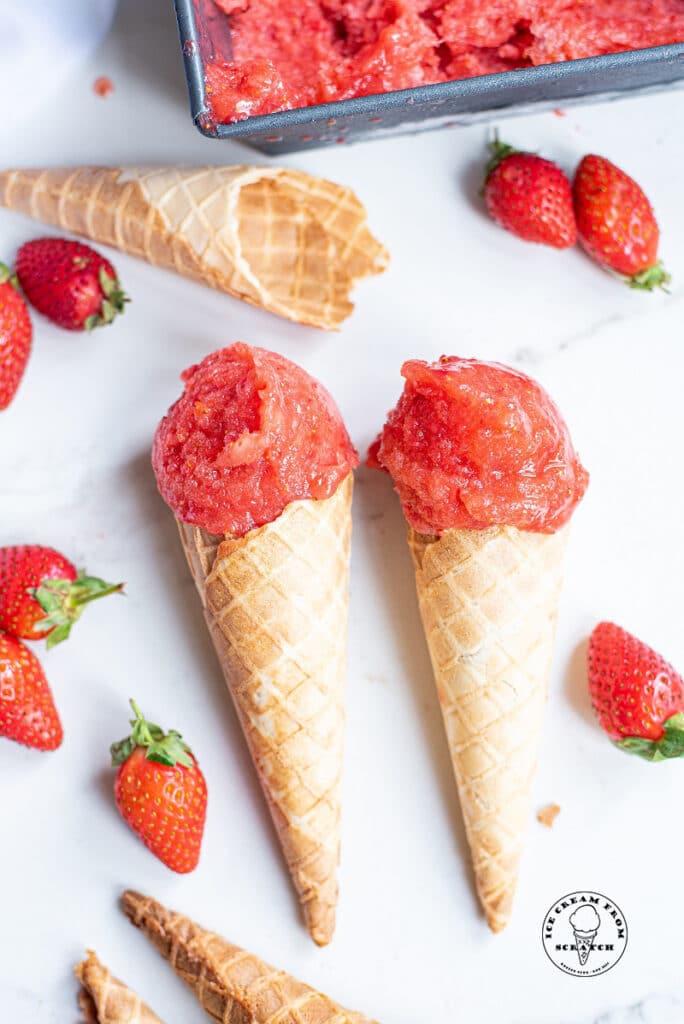 two ice cream cones with scoops of strawberry sorbet on top