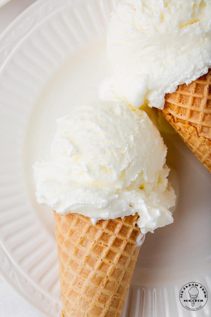 closeup view of two sugar cones of sweet cream ice cream on a white plate.