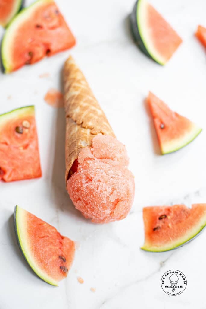 a scoop of watermelon sorbet in an ice cream cone next to slices of watermelon