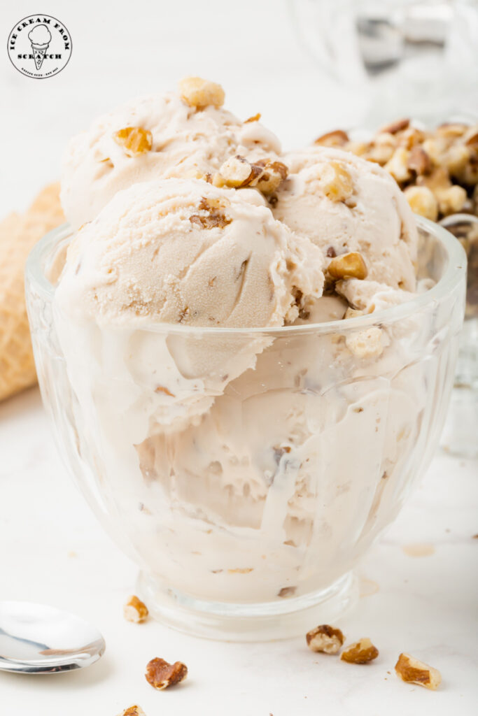 black walnut ice cream, multiple scoops in a glass ice cream dish, topped with chopped walnuts.