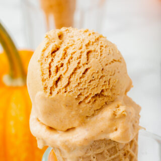 a sugar cone with a scoop of pumpkin spice ice cream, propped up in a glass. There is a pumpkin in the background.