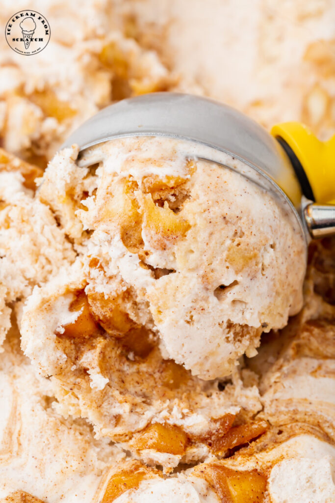 Ice cream with cinnamon and apple pie pieces being scooped with a metal ice cream scoop. Close up shot.