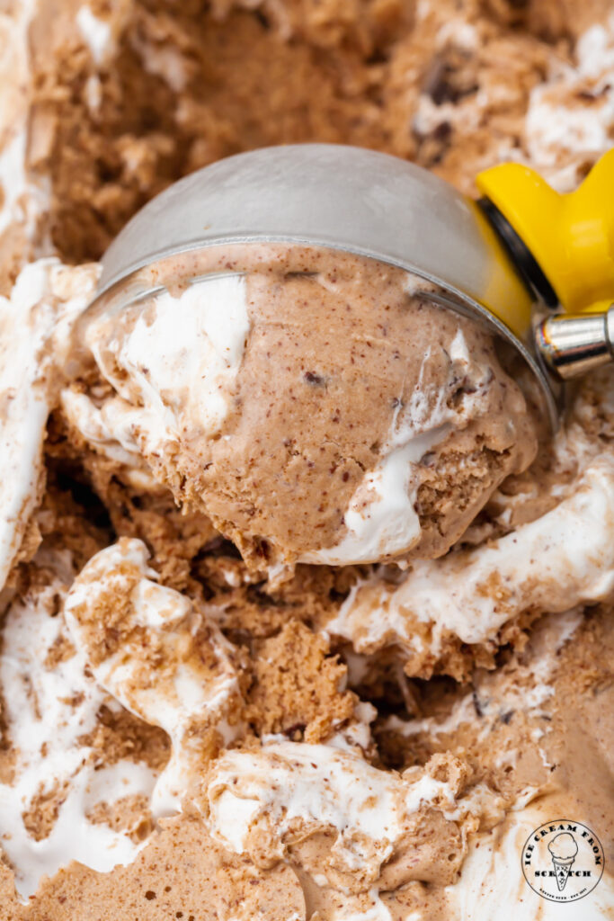 a metal ice cream scoop, scooping through chocolate ice cream with marshmallow swirls