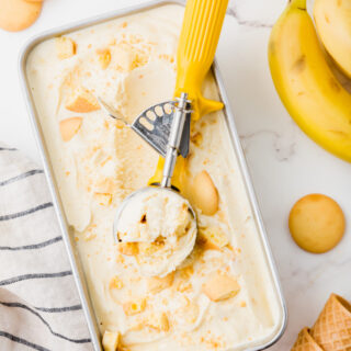 a metal pan filled with banana ice cream topped with vanilla wafers being scooped with a yellow ice cream scoop.