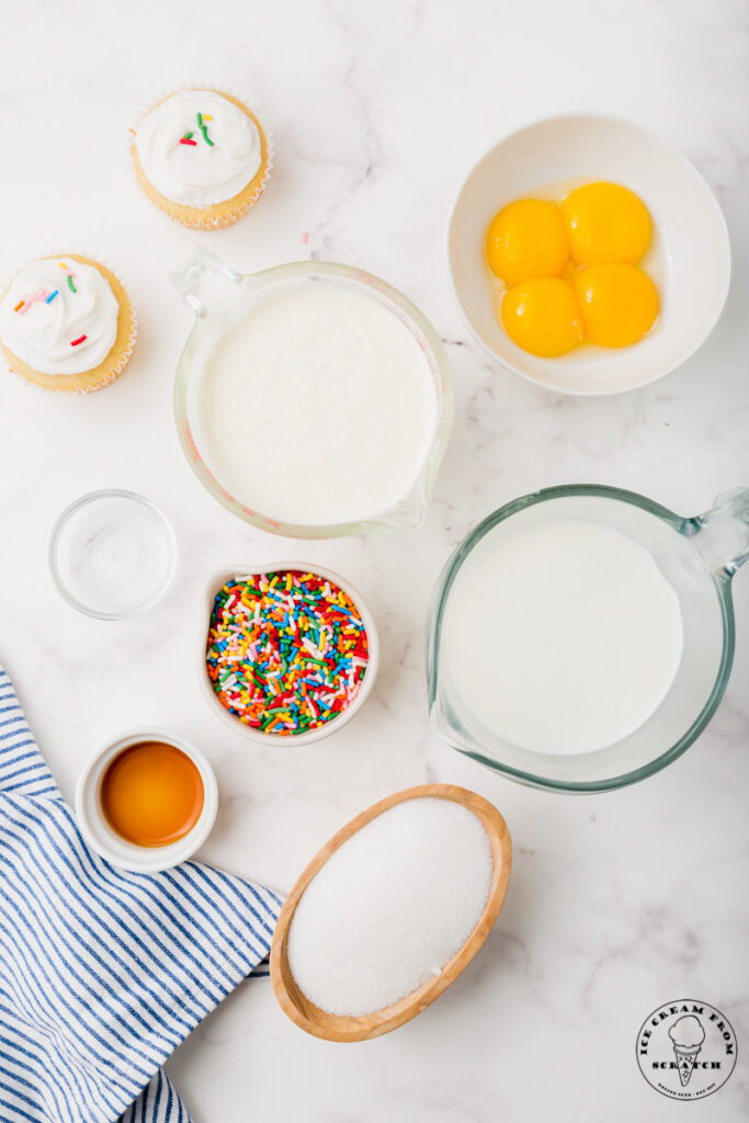 top down view of the ingredients needed to make birthday cake ice cream including egg yolks, cream, sprinkles, and cupcakes.