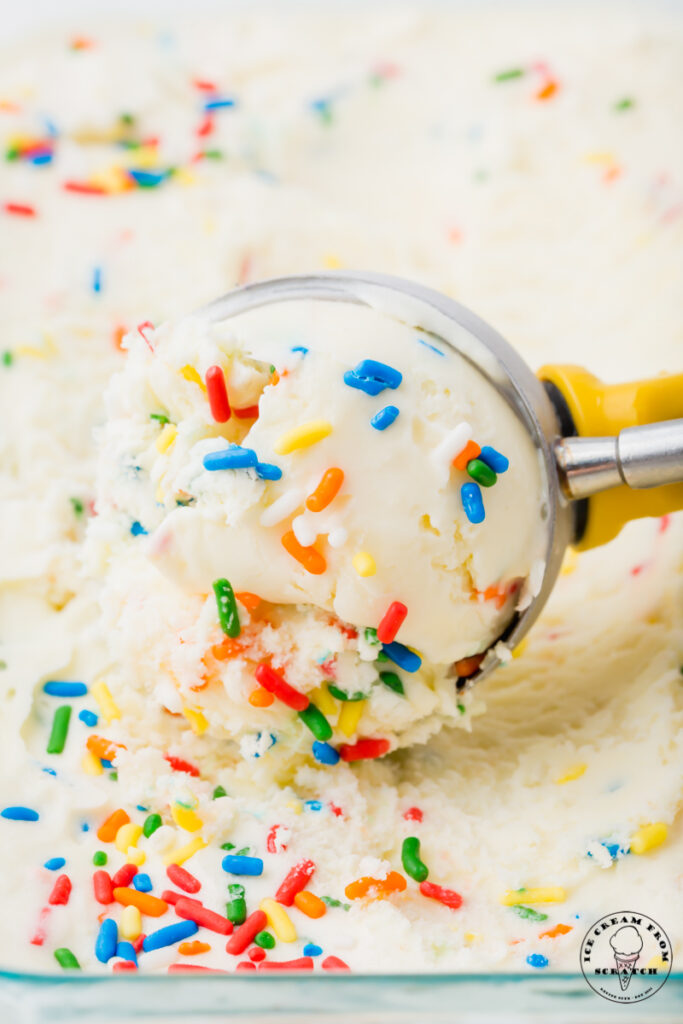 a metal ice cream scoop with a yellow handle, scooping ice cream with sprinkles in it.