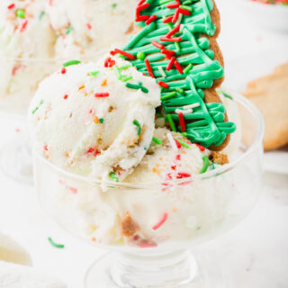 a wide, short, glass ice cream dish with scoops of christmas ice cream and a green frosted tree cookie topper.