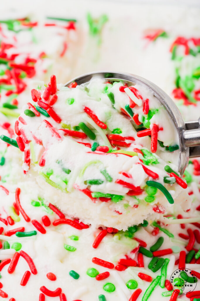 vanilla ice cream topped with red and green christmas sprinkles being scooped by a large ice cream scoop