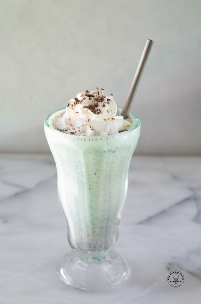 mint chocolate chip milkshake in a clear glass with a metal straw