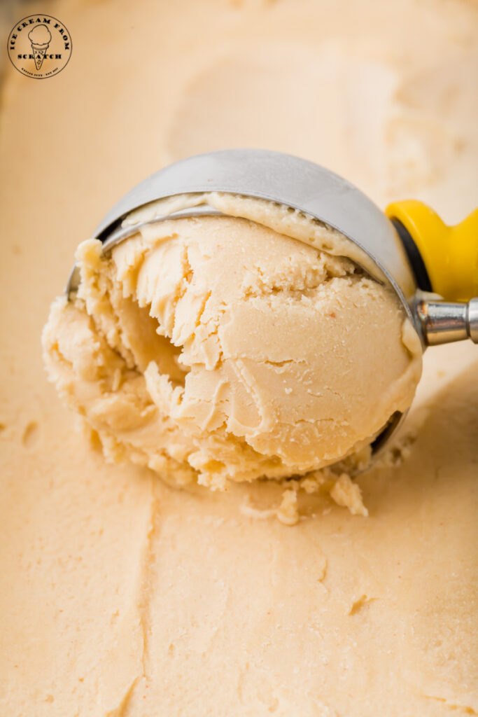 a metal ice cream scoop with a yellow handle scooping peanut butter ice cream.