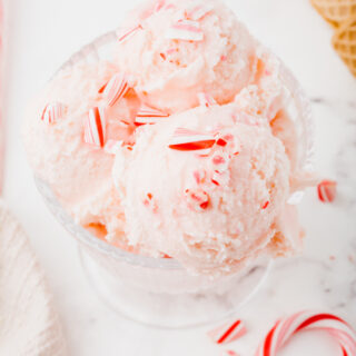 a glass bowl filled with scoops of pink ice cream. Crushed candy canes top the ice cream.