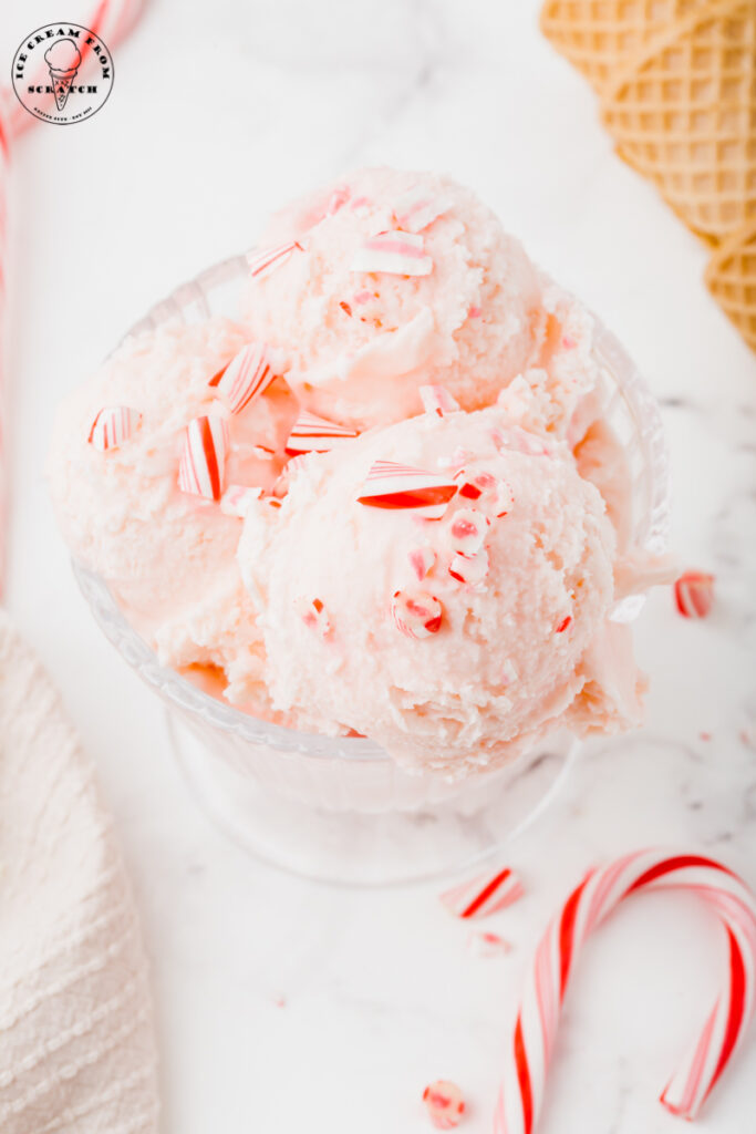 a glass bowl filled with scoops of pink ice cream. Crushed candy canes top the ice cream.