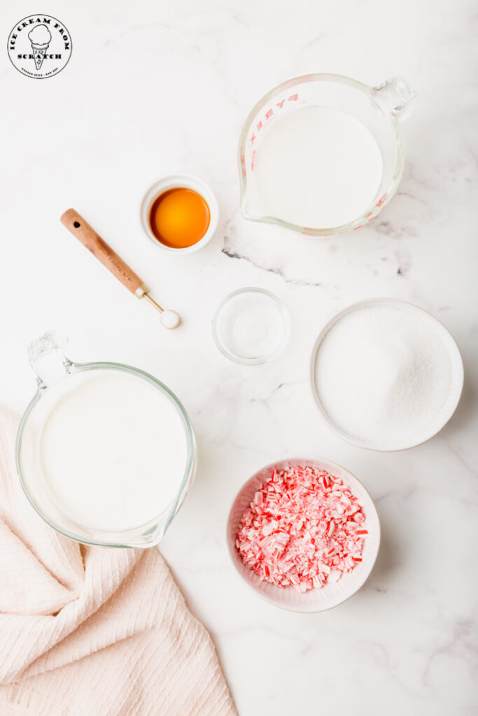 Ingredients for peppermint stick ice cream are laid on a marble countertop in separate bowls. Just 6 ingredients, including crushed candy canes, sugar, and cream.