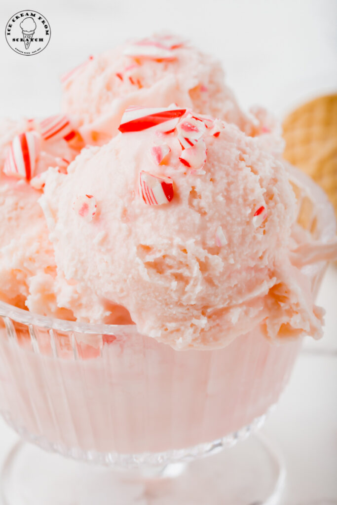 closeup view of a glass ice cream dish filled with scoops of pink peppermint ice cream with crushed candy canes on top