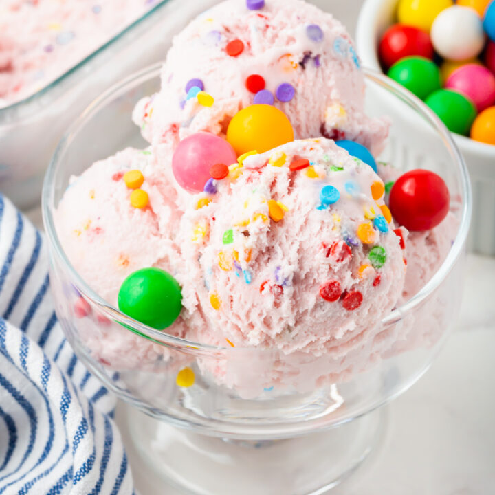 A glass dish of pink bubblegum ice cream with rainbow sprinkles and garnished with gum balls.