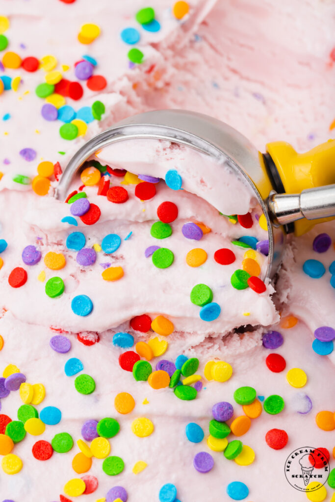 a metal ice cream scoop is scooping pink bubblegum ice cream.