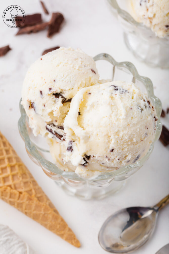 a footed glass dessert dish is filled with scoops of homemade chocolate chip ice cream