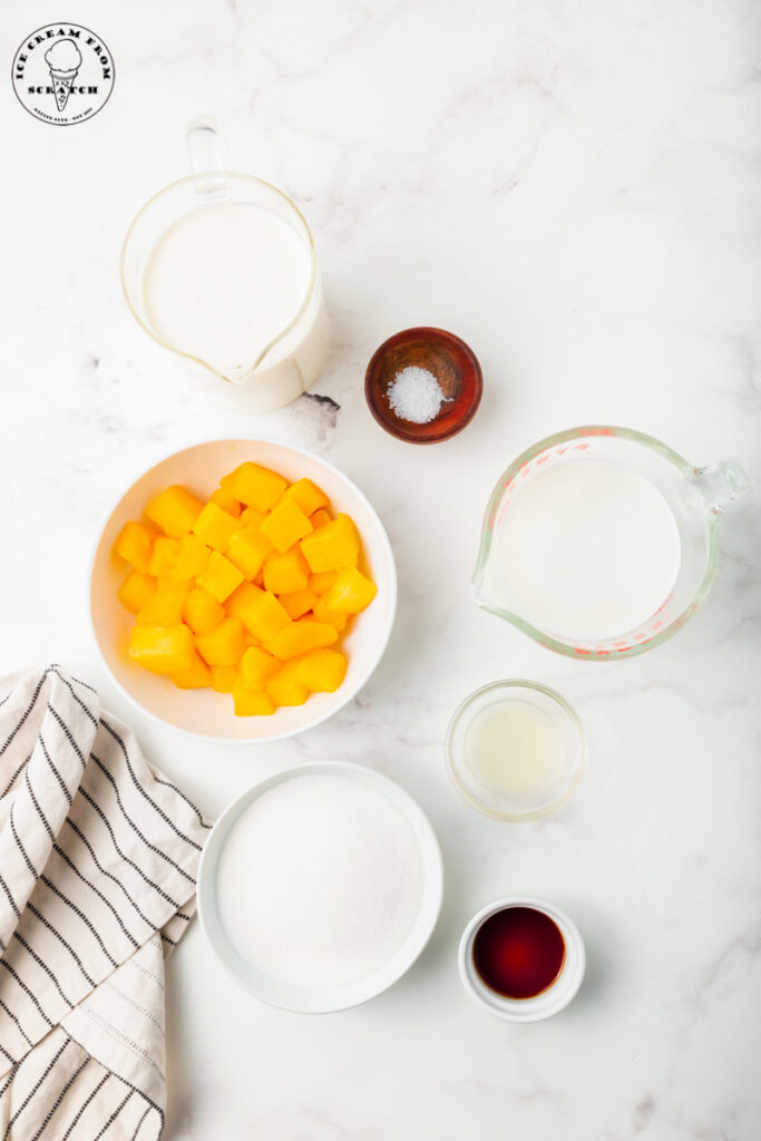 Ingredients for homemade mango ice cream on a marble countertop all in separate bowls.