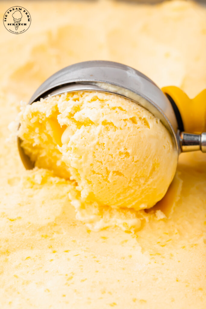 a metal ice cream scoop creating a scoop of mango ice cream, close up.
