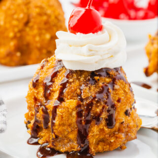 A single scoop of fried ice cream topped with chocolate syrup, whipped cream, and a marachino cherry