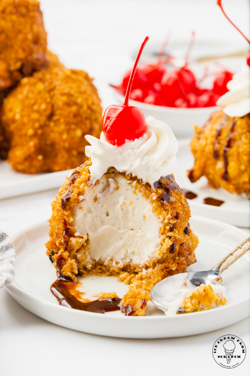 a serving of fried ice cream that has had a few bites taken out. Inside the fried ice cream is creamy vanilla, on top is whipped cream and a cherry.