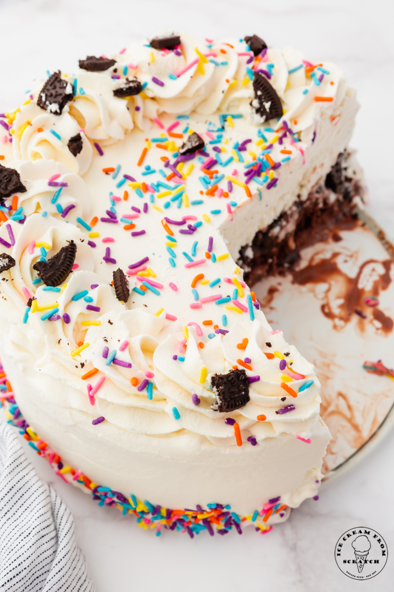 top view of a round cream cake decorated with sprinkles that has had 3 slices removed.