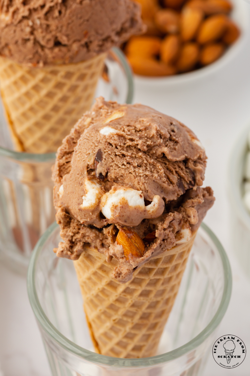 a sugar cone with a scoop of homemade rocky road ice cream is propped up in a glass.