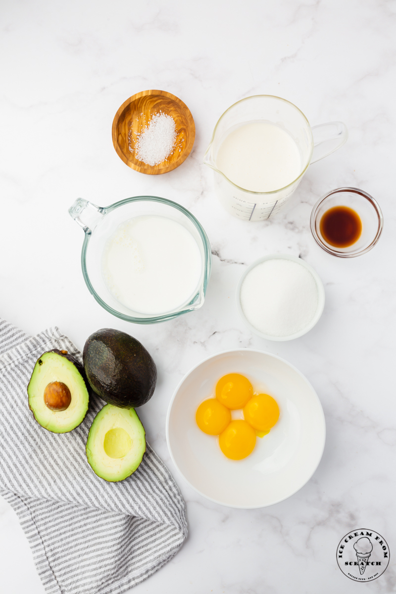 A collection of bowls on a marble counter top, each filled with an ingredient needed for making avocado ice cream