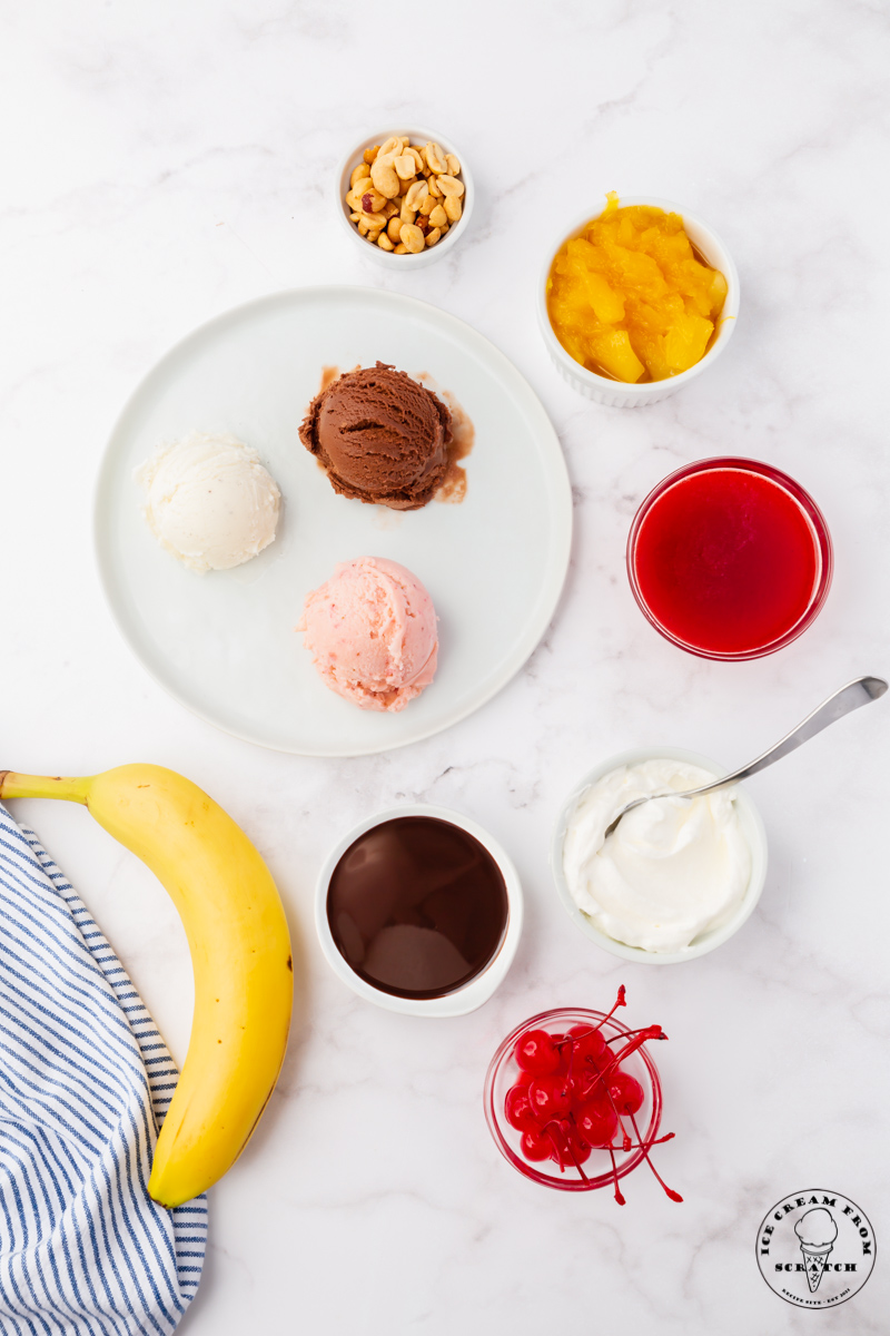 The ingredients for making a traditional ice cream sundae, all in separate bowls on a marble countertop. 