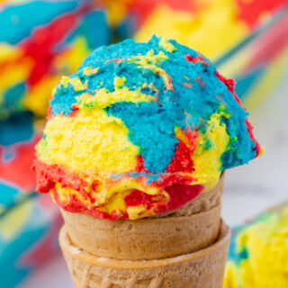 a sugar cone topped with a scoop of brightly colored yellow, blue, and red superman ice cream.