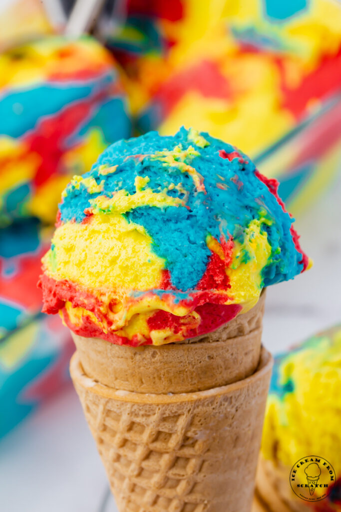 a sugar cone topped with a scoop of brightly colored yellow, blue, and red superman ice cream.