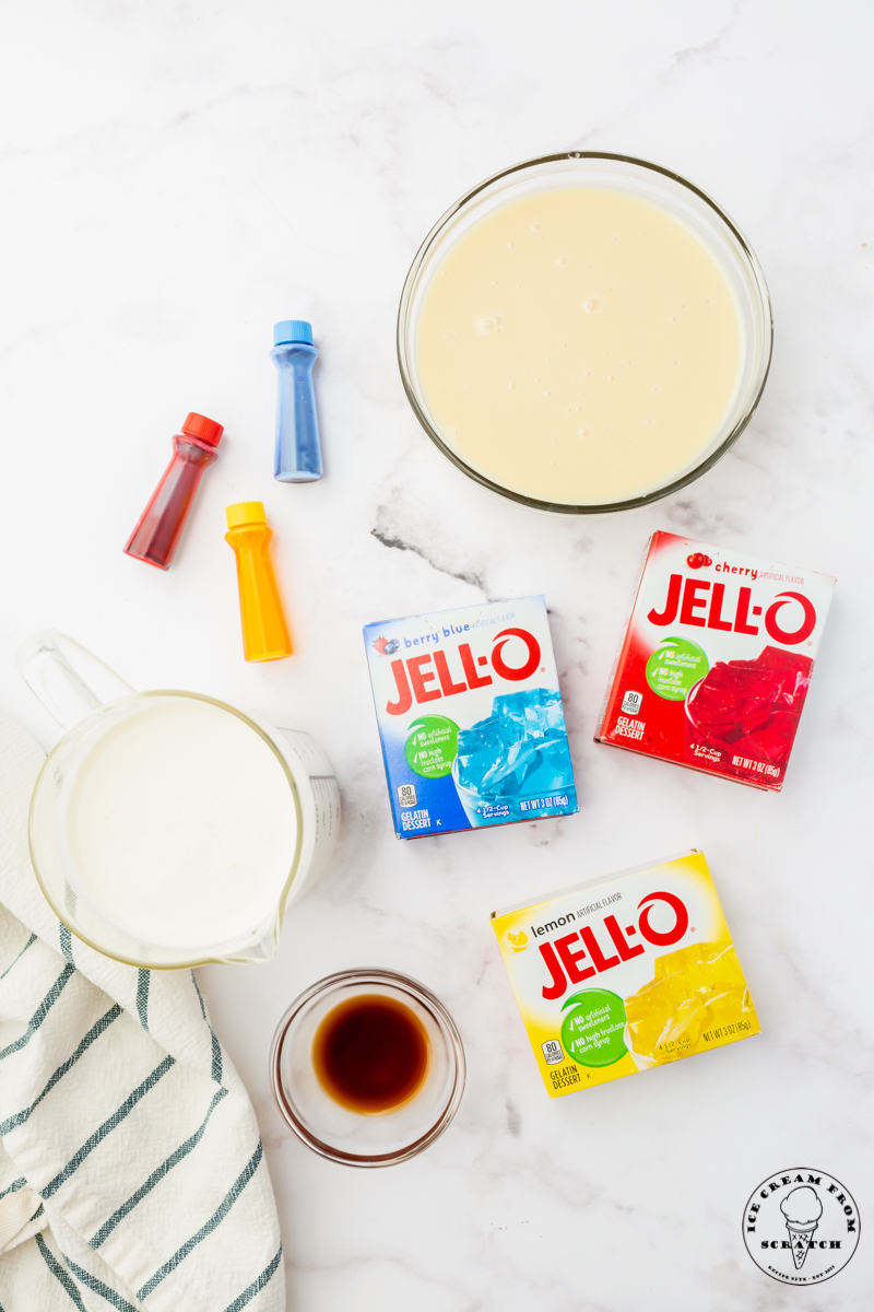 The ingredients for no churn superman ice cream on a marble counter, including cream, food coloring, and jello