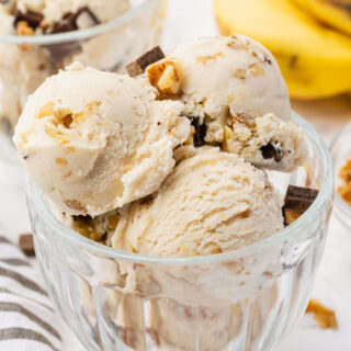 a glass bowl filled with 4 scoops of homemade chunky monkey ice cream topped with chocolate chunks and walnuts