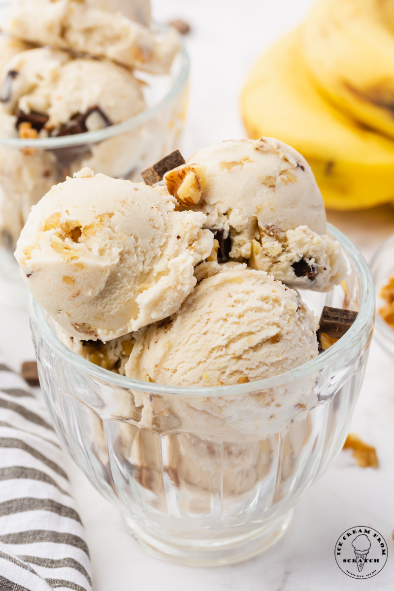 a glass bowl filled with 4 scoops of homemade chunky monkey ice cream topped with chocolate chunks and walnuts