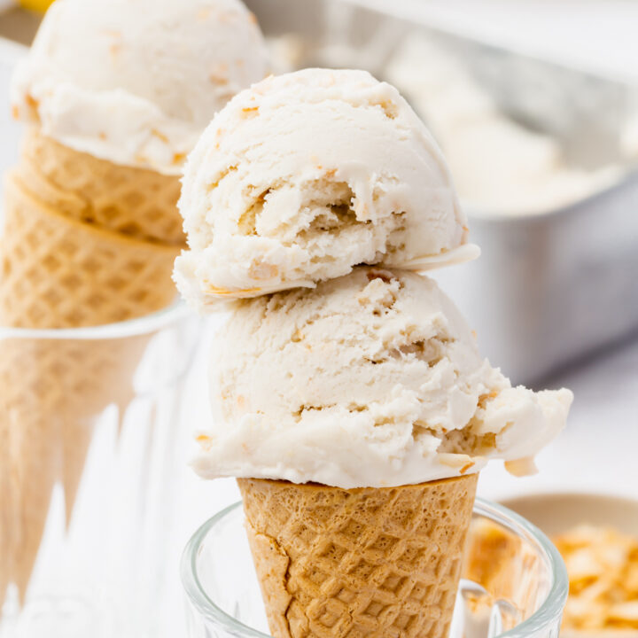a sugar cone propped up in a glass topped with two scoops of homemade coconut ice cream. another cone sits in the background.