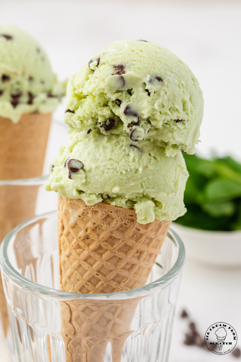 a sugar cone propped up in a glass, topped with two scoops of mint chocolate chip ice cream.