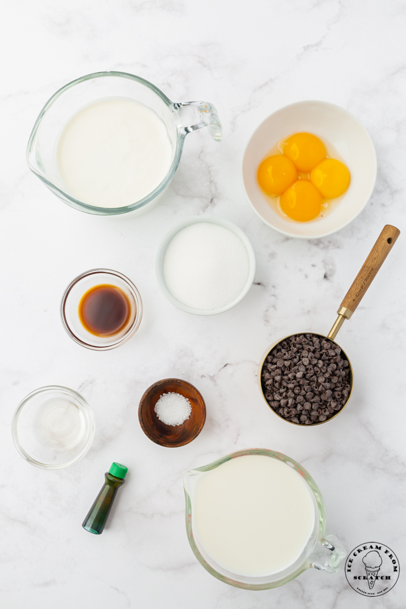 The ingredients for mint chocolate chip ice cream, measured into separate bowls and set on a marble counter, viewed from above.